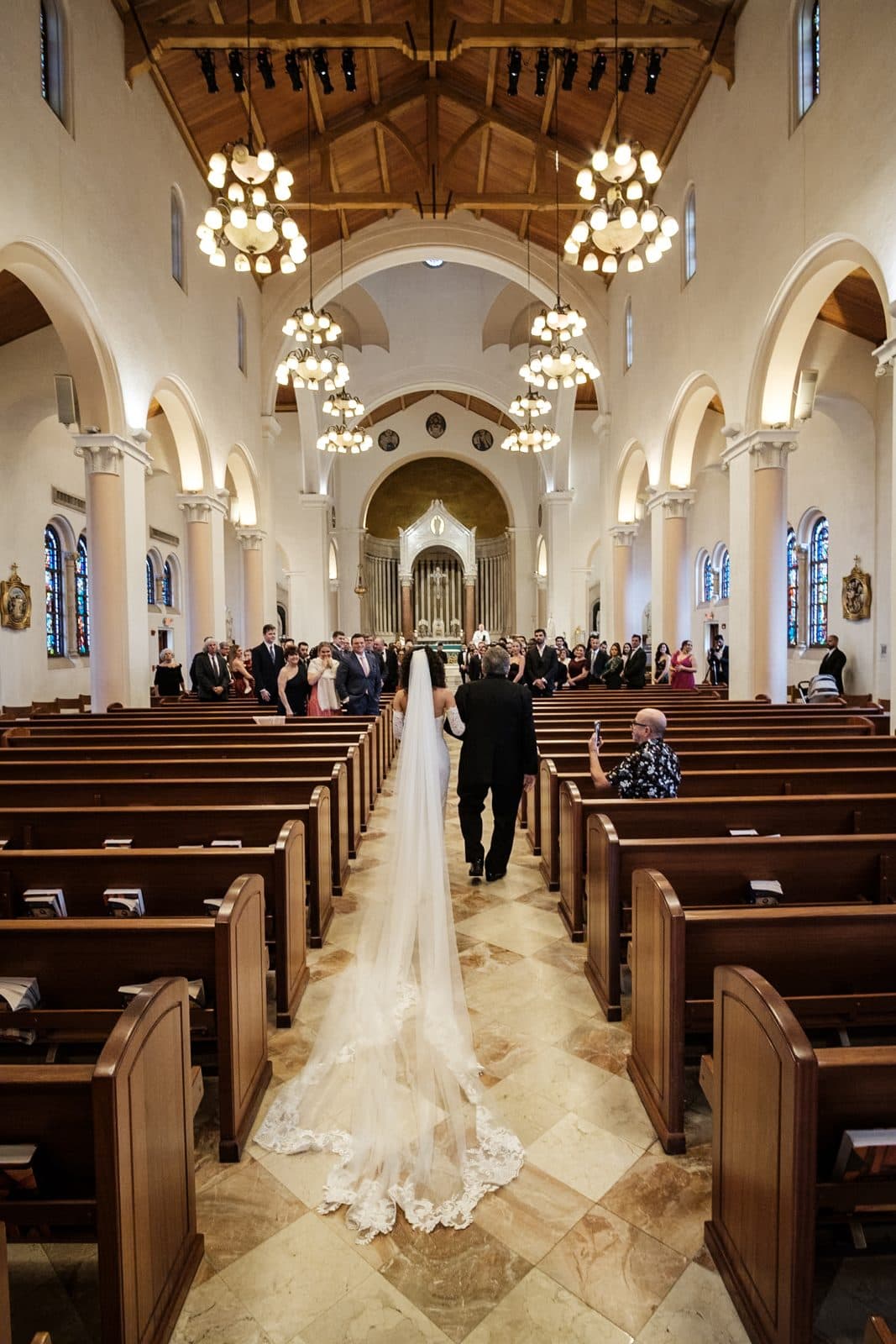 A bride walking the ceremony aisle as guests stand in church pews